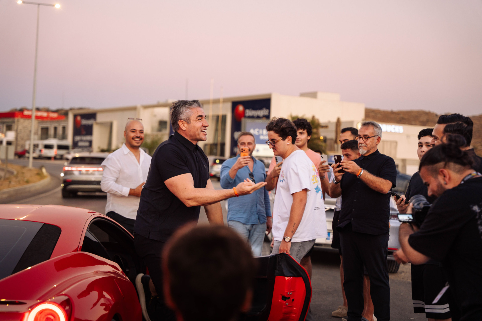 The Noizy Boyz crew greeting the crowd beside a red sports car at dusk