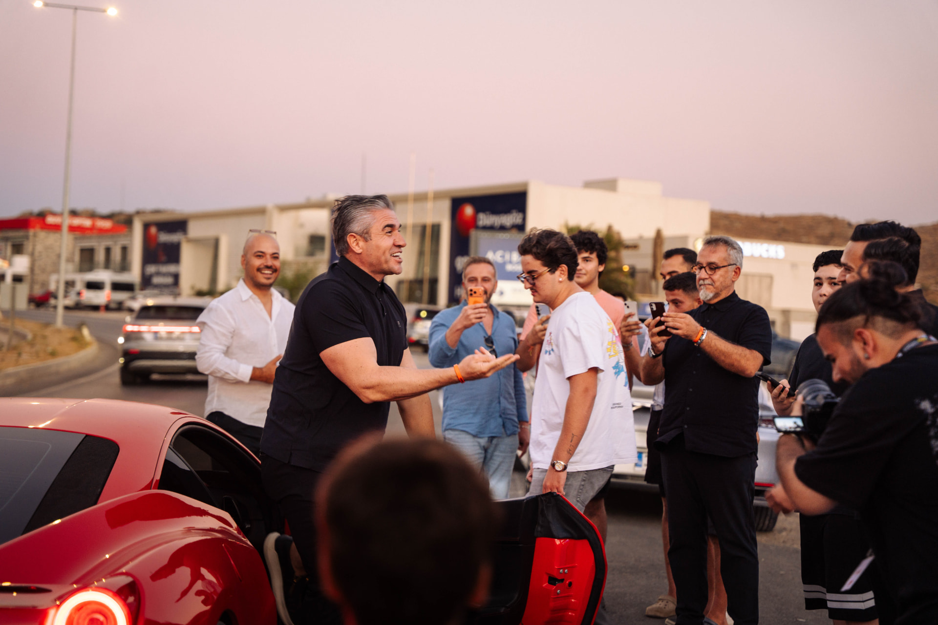 Friends gathered around a red Ferrari at golden hour