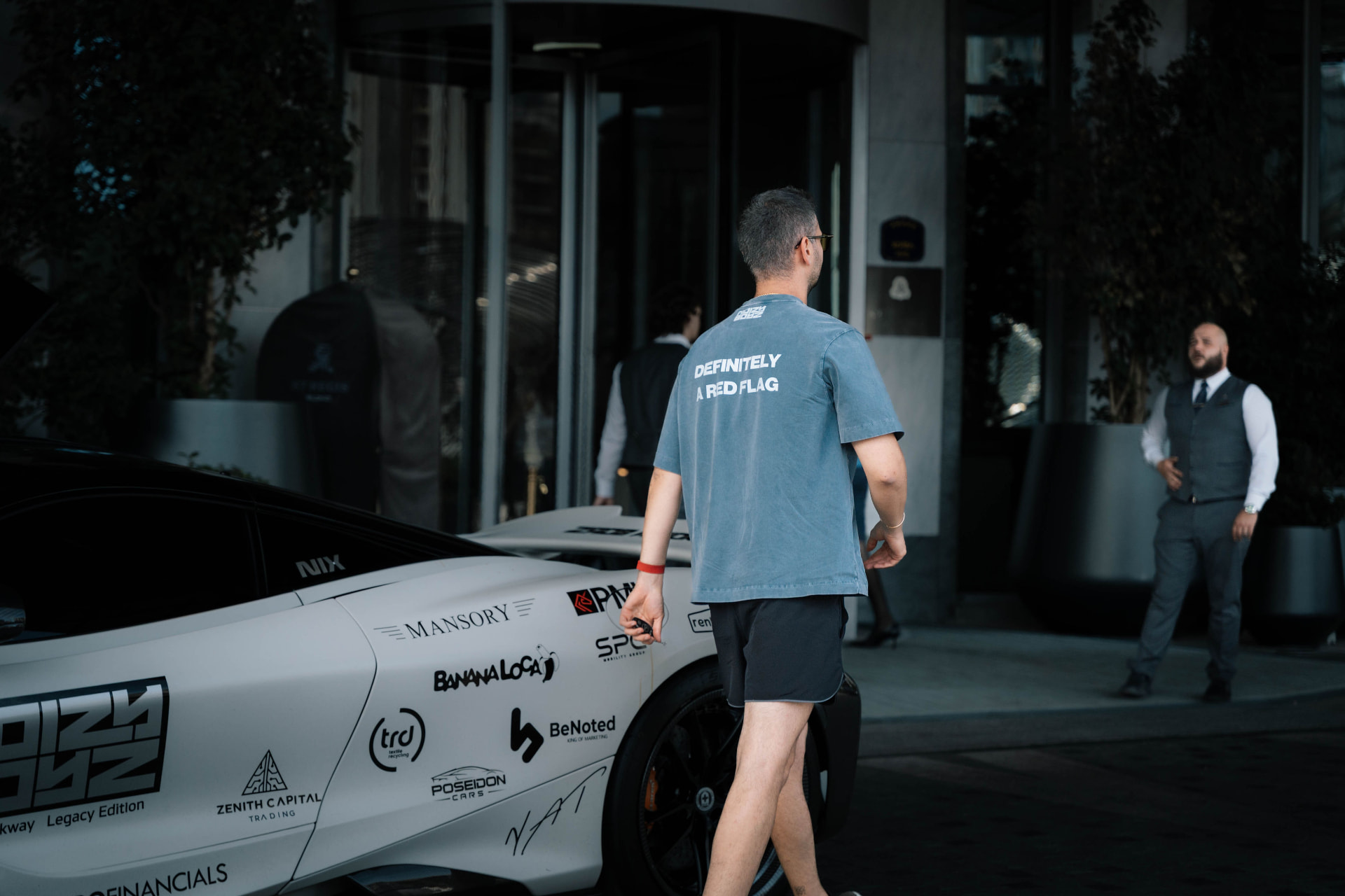 Blue Noizy Boyz shirt reading Definitely a red flag beside a white McLaren