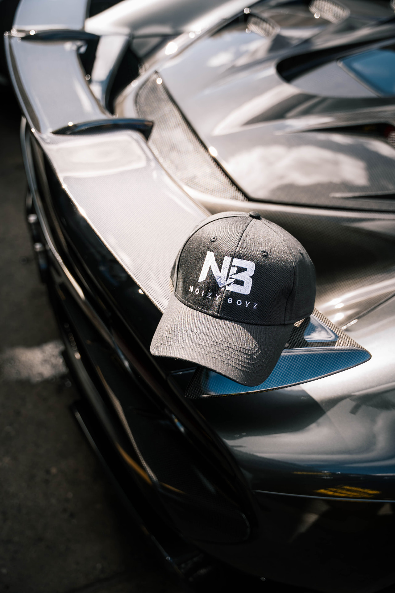 A Noizy Boyz cap resting on a supercar